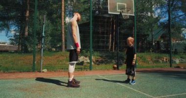 Basketbolcular antrenmandan önce ısınma egzersizi yapıyorlar. Sportif aile babası ve oğlu basketbol sahasında antrenman yapıyor. 