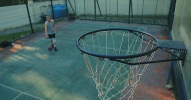 Basketbolcu genç adam basketbol sahasında antrenman yapıyor. Topu potaya atıyor.