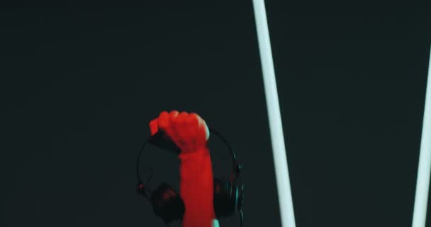Tangan laki-laki dengan headphone mengangkat dalam cahaya penuh warna pada bergerak lampu latar belakang, close-up. Konsep musik dan protes — Stok Video