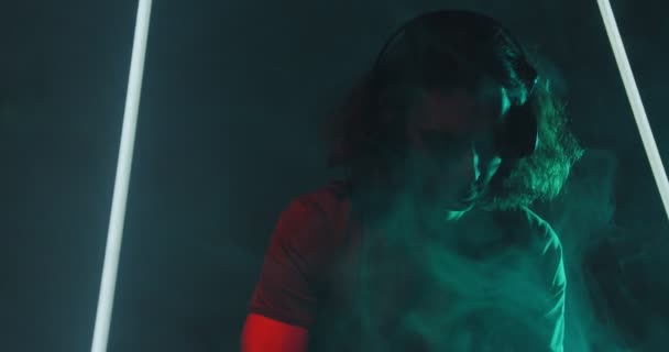 Cool deejay jonge langharige man met koptelefoon in rook op het feest in de nachtclub — Stockvideo