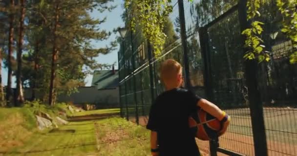 Basketbalspeler kind jongen met bal gaat naar training op basketbalveld en scoren hoepel buiten in de zomer — Stockvideo