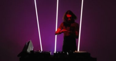 DJ 'lik yapan havalı adam gece kulübündeki performans sırasında pikabın ışıklarında dans ediyor. Modern parti