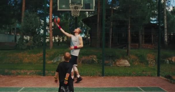 Jugador de baloncesto masculino padre entrenamiento niño su hijo para anotar aro lanzar pelota en la canasta en la cancha de baloncesto al aire libre — Vídeos de Stock
