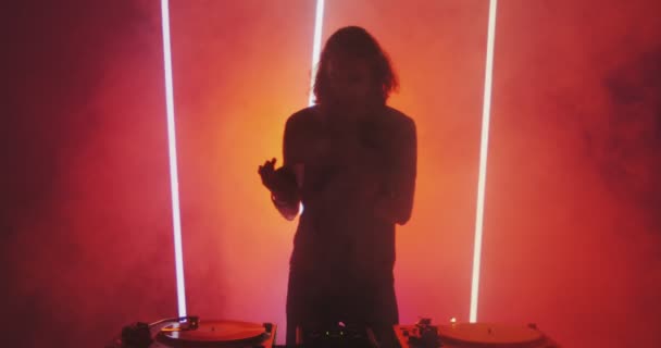 Silhouette di deejay cool giovane ragazzo che suona musica sul giradischi a luce rossa in fumo in discoteca — Video Stock