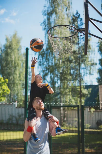 Familia feliz jugando baloncesto. Joven padre deportivo con hijo en hombros. Niño lanzar pelota en baloncesto aro al aire libre — Foto de Stock