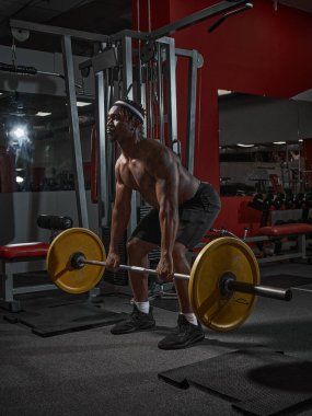 Spor salonundaki antrenman sırasında güçlü Afrikalı Amerikalı adam halterle çömeliyor. Kilo verme egzersizi