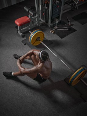 Spor salonunda halterle antreman yapan çıplak gövdeli Afrikalı Amerikalı bir adam yerde dinleniyor. Üst görünüm