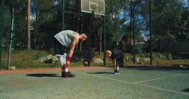 Basketbolcular antrenmandan önce ısınma egzersizi yapıyorlar. Sportif aile babası ve oğlu basketbol sahasında antrenman yapıyor. 