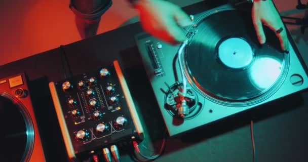 Deejay memainkan musik elektronik di meja putar di pesta klub malam dengan cahaya berwarna-warni. Dj menyentuh vinil, sliders. Tampilan atas — Stok Video