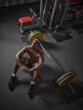 Yakışıklı kaslı atletik Afrikalı Amerikalı adam spor salonunda halterle yerde yatıyor. Kuvvetli eğitim kavramı