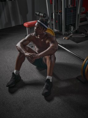 Kas yığını atletik Afrikalı Amerikalı adam spor salonunda halterle yerde oturuyor. Kuvvetli çalışma kavramı