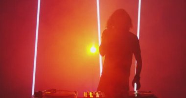 DJ gece kulübünde sahne alıyor mikser kontrolöründe, dans ediyor, kırmızı ışıkta sallanıyor. Gece hayatı konsepti
