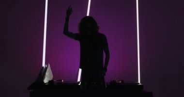 Silhouette of Dj performing, dancing at mixer controller, rocking party up in nightclub. Nightlife concept