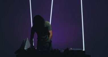 Cool young male deejay performing in nightclub, playing vinyls at mixer controller, rocking party up. Nightlife concept