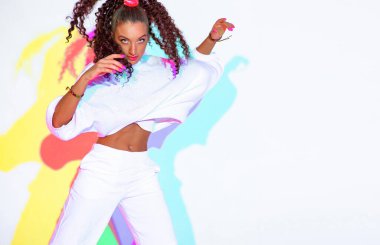 Güzel dans eden karışık ırk saçı beyaz arka planda renkli neon renkli stüdyo ışığı olan genç kız, boşluğu kopyala