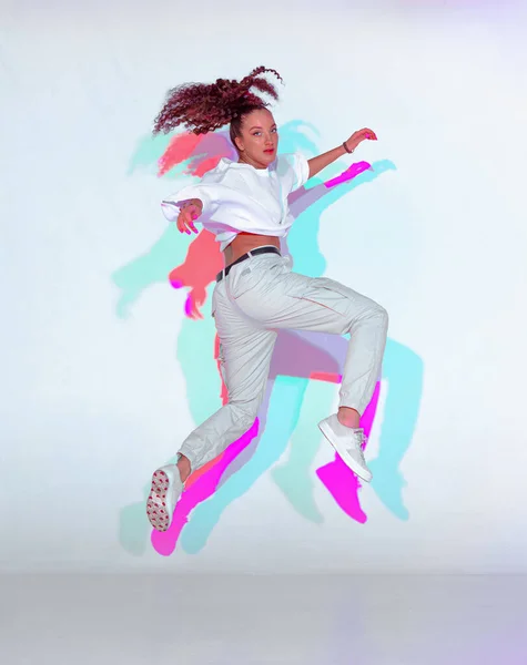 Salto de raza mixta joven danza en la luz de colores. Bailarina performer jump dancing fiery hip hop — Foto de Stock