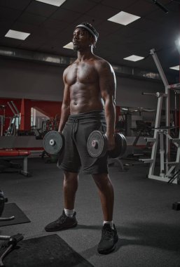 Spor salonunda kaslı Afrikalı Amerikalı vücut geliştirme uzmanı. Dambılı yakışıklı atletik adam.
