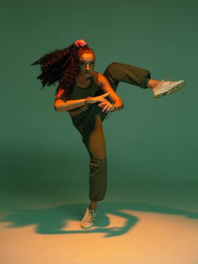 Afro saçlarıyla karışık dans eden kız renkli stüdyo ışığı altında etkileyici hip hop dansı yapıyor.