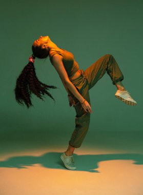 Dans eden atletik melez kız stüdyo ışığında ateşli hip hop ya da etnik afro dansı yapıyor.