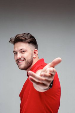 Mutlu, dost canlısı, başarılı, gülümseyen genç adam el ele fotoğraf çekiyor. Stüdyo resmi gri arka planda, fotokopi alanı ile birlikte.