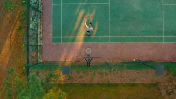 Vista aérea del jugador de baloncesto acercándose, anotando aro durante el entrenamiento en la cancha de baloncesto al aire libre a la luz del sol — Vídeos de Stock