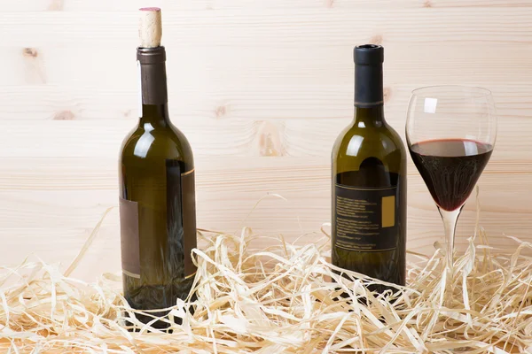 Dos botellas de vino tinto y una copa de vino en paja — Foto de Stock
