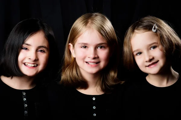 Drei kleine Mädchen posieren auf schwarzem Hintergrund — Stockfoto