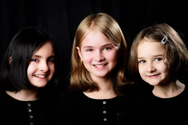 Three little girls posing on a black background — Stock Photo, Image