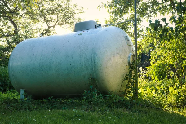 Propane tank in a backyard surrounded by green trees and grass on a spring evening in Potzbach, Germany.