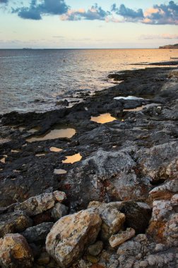 Mellieha, Malta 'da gün batımında plajdaki kaya havuzlarında turuncu yansımalar..