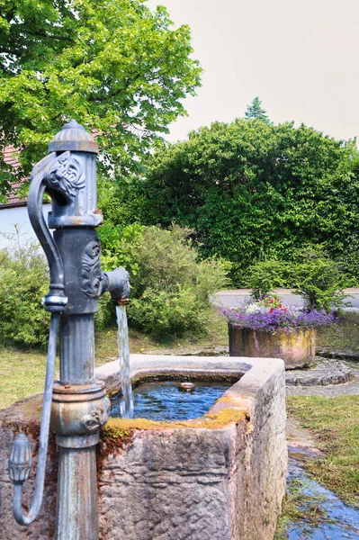 Back of a decorative water pump with running water at a park in Potzbach, Germany.