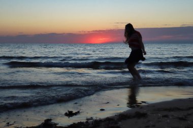 Gün batımında Malta 'da bir sahilde suya atlayan bir kızın silueti..