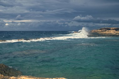 Fırtına bulutları dalgaların üzerinden okyanusta kayalara çarpıyor Qawra, Malta 'da.
