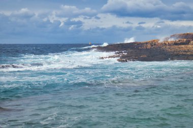 Bulutlu bir günde, Qawra, Malta 'da bir plajda okyanusta su kıvrılıyor..