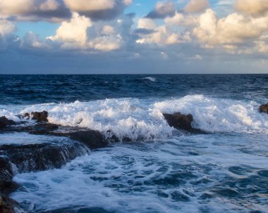 Mavi okyanustaki kayaların üzerinden akan beyaz su Qawra, Malta 'da bir sonbahar akşamında.
