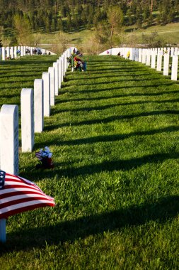 Sturgis, Güney Dakota - 27 Mayıs 2022: Güney Dakota 'da güneşli bir bahar akşamında Black Hills Ulusal Mezarlığı' ndaki yeşil çimlerin üzerindeki mezar taşlarından gölgeler.