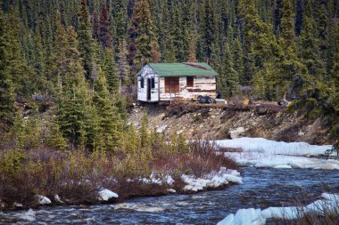 Bir bahar günü Denali otobanındaki bir nehirde dökülen eski bir ahşap kulübe...