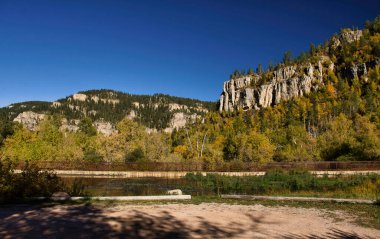 Güneşli bir sonbahar gününde, Güney Dakota 'da Spearfish Kanyonu' nda mavi gökyüzü olan bir köprüde renkli ağaçlarla dolu bir tepede kireçtaşı kayaları..
