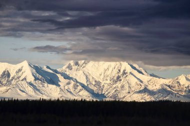 Alaska 'daki Denali Otoyolu' nda bir bahar günü karlı bir dağın tepesini kaplayan kara bulutlar.. 