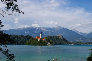 Bled, Slovenya - 30 Temmuz 2021: Gölde Meryem Ana Kilisesi 'nin arkasındaki dağlar ve Slovenya' da güneşli bir yaz günü Castle Bled oon.