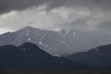 Alaska 'da yağmurlu bir bahar gününde Denali otobanındaki dağların üzerinden sis ve kara bulutlar..