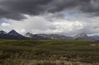 Alaska 'daki Denali Otoyolu' nda bir bahar günü, kara bulutların altında güneş parlıyor..