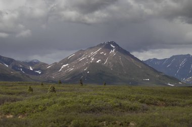 Alaska 'daki Denali Otoyolu' nda bir bahar günü, kara bulutların altında güneş parlıyor.. 