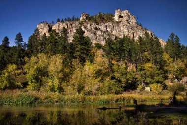 Güney Dakota 'da güneşli bir sonbahar gününde Spearfish Kanyonu' ndaki kayalıkların altında su ve renkli ağaçlar..