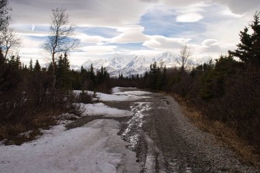 Kömür madeni yolunda kar eriyor. Arka planda karlı dağlar var. Delta Kavşağı, Alaska yakınlarında bir bahar günü..