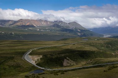 Alaska Boru Hattı 'nın arkasındaki dağlarda parlayan güneş bulutlu bir yaz gününde Alaska' nın iç kesimlerinde.