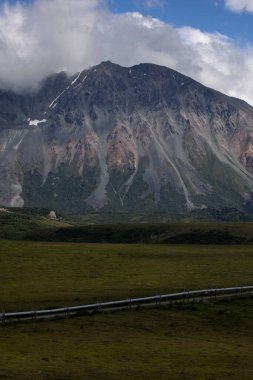 Alaska 'daki Richardson Karayolu yakınlarındaki bir yaz gününde boru hattının üzerindeki dağların üzerinden beyaz bulutlar..