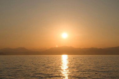 İtalya 'da bir yaz akşamı gün batımında Garda Gölü' nün arkasındaki dağların üzerinden güneş..