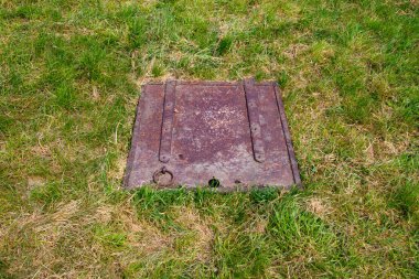 Çim tarlasında eski paslı bir metal karenin kapağını kapatın.