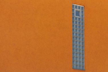 Turuncu duvarda cam bloklar olan dikey pencere.